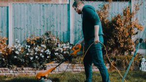 Man Holding Orange Electric Grass Cutter On Lawn | Common Gardening Mistakes And Tips On How To Avoid Them | Featured